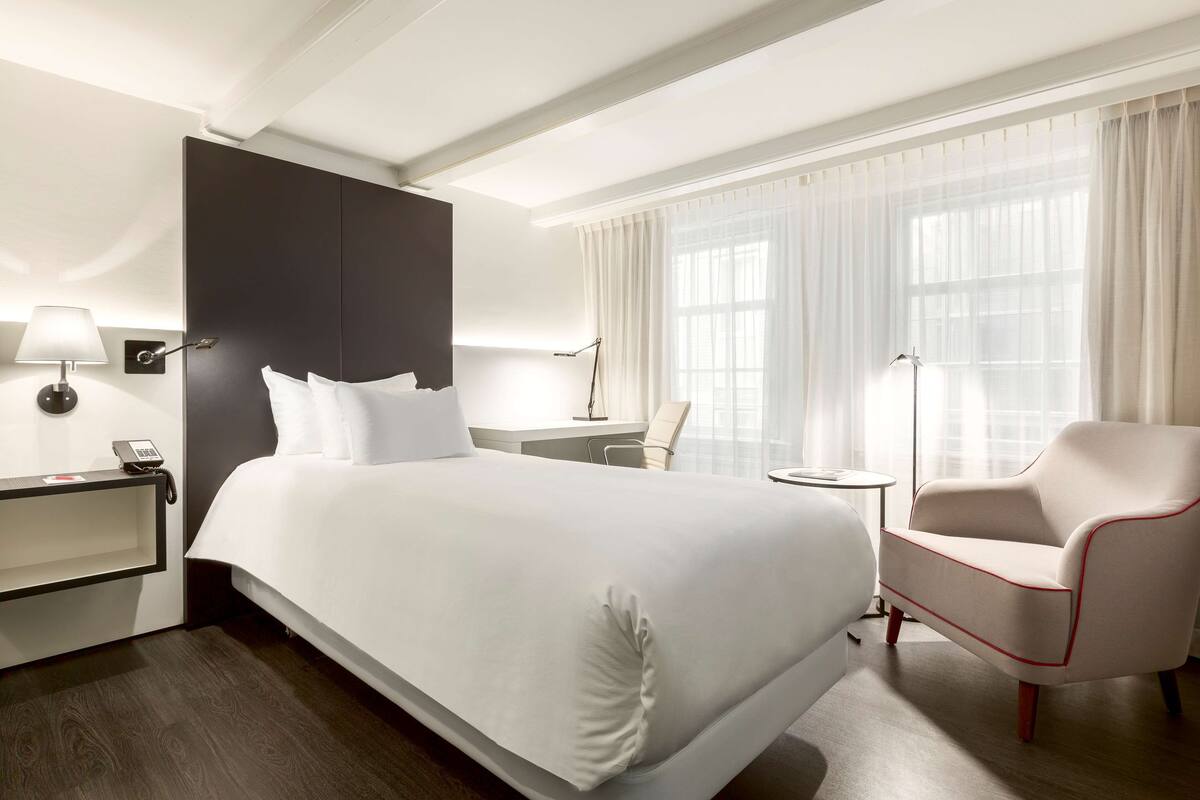 A hotel room with a large bed, a desk, a chair, and a lamp.