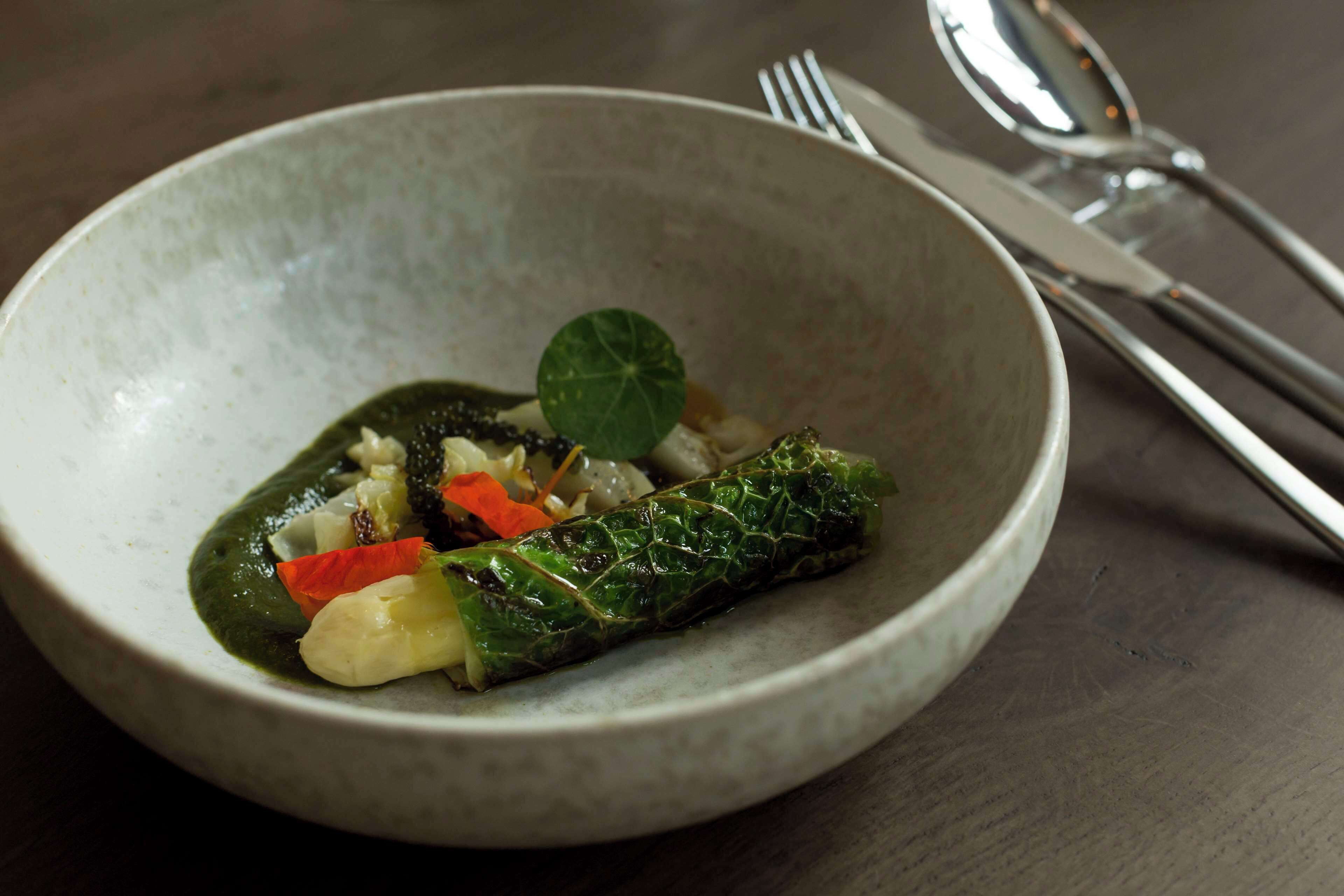 Een kom met eten, met een gerold groentegerecht, mogelijk een zuurkoolrolletje, en diverse groenten zoals wortelen en bloemkool.