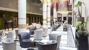 A spacious lobby with modern seating, a large chandelier, and decorative plants. - NH Collection Amsterdam Barbizon Palace (Amsterdam)