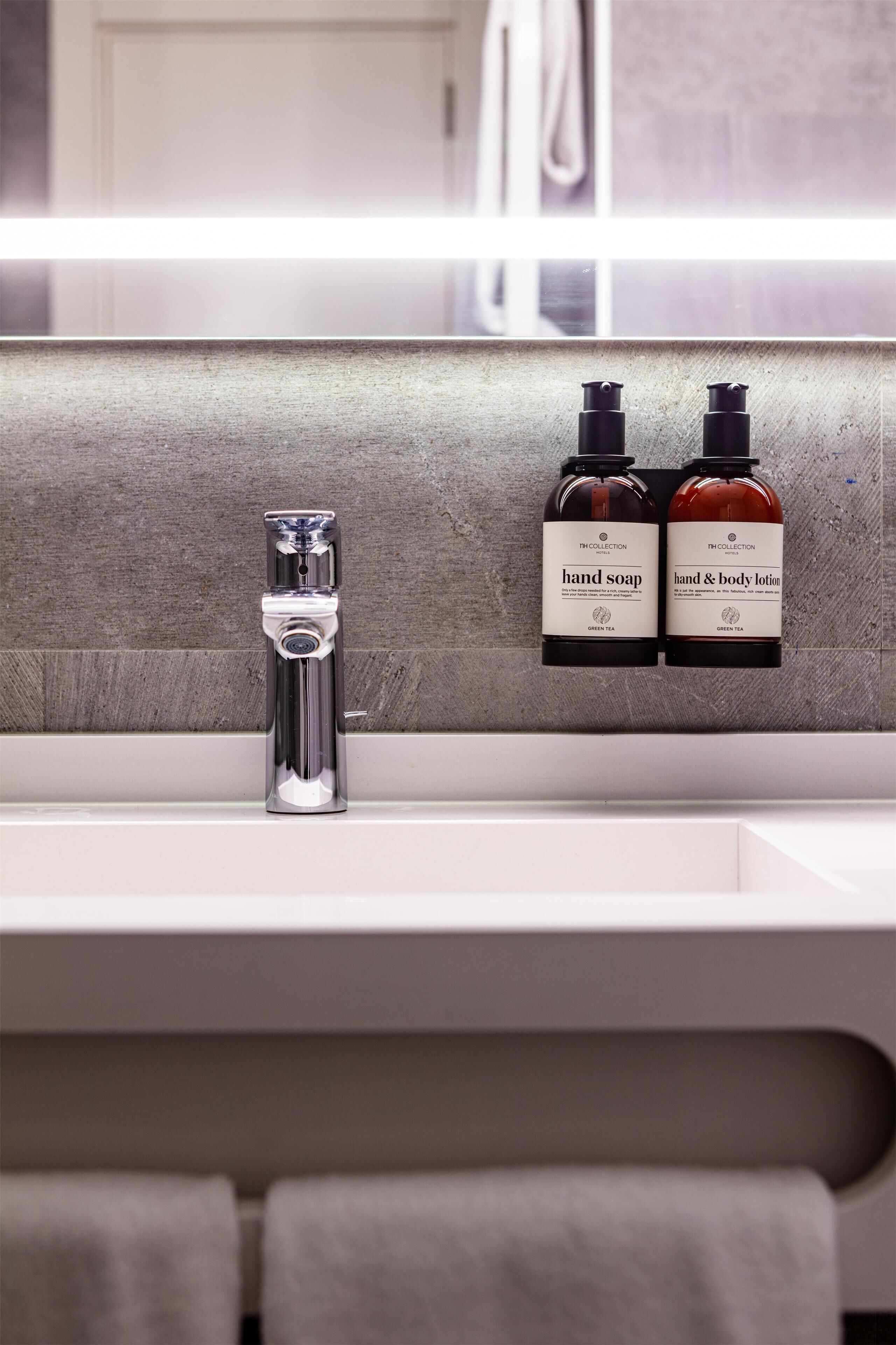 A bathroom with a modern sink, two bottles of hand soap and body lotion, and a faucet.