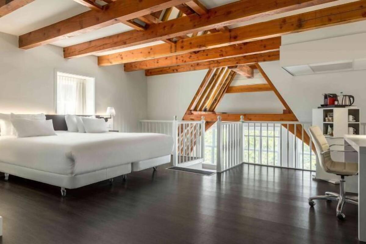 A bedroom with a large bed, a desk, and a view through a window.