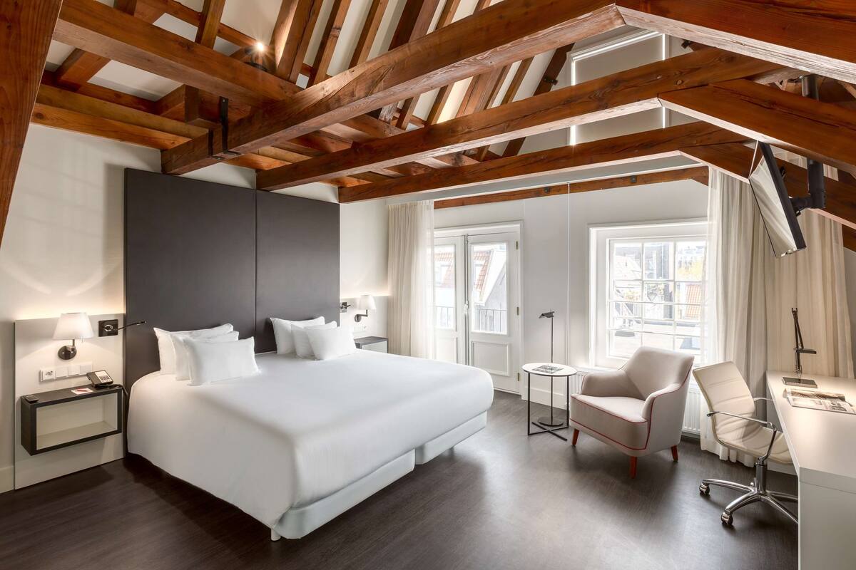 A modern hotel room with a large bed, a desk, and a chair.