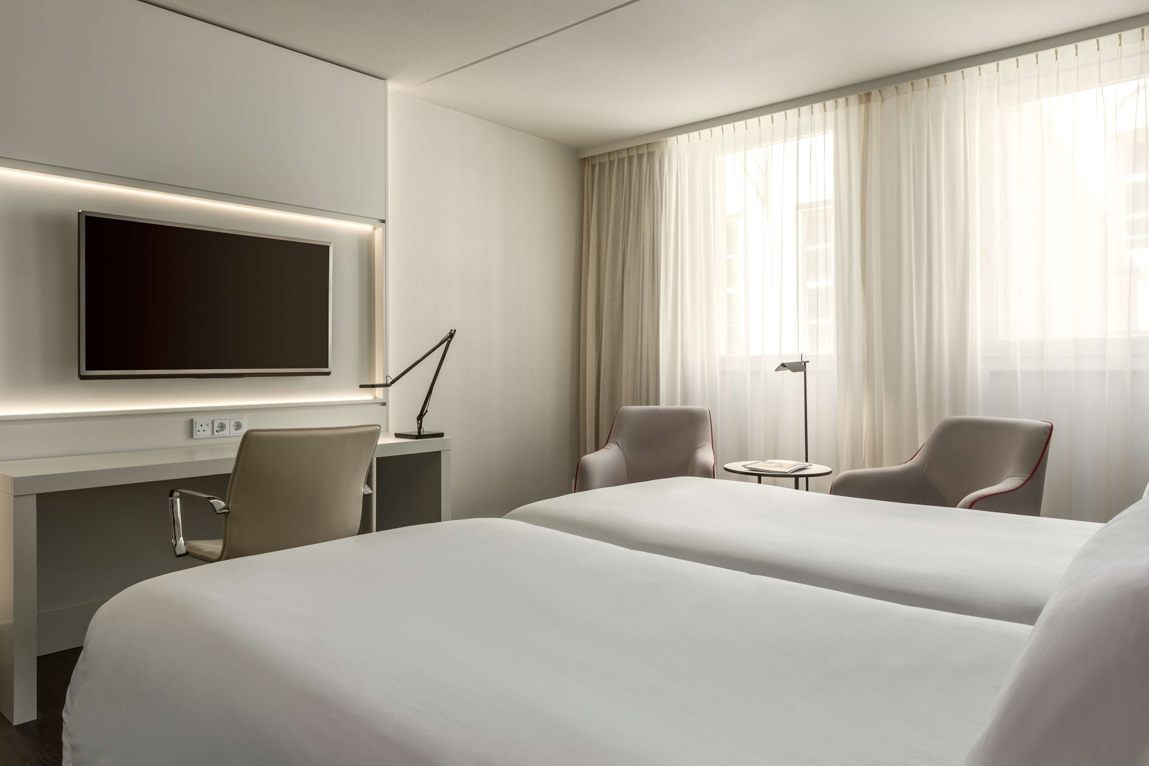 A hotel room with two beds, a desk with a flat-screen TV, a lamp, and a chair.