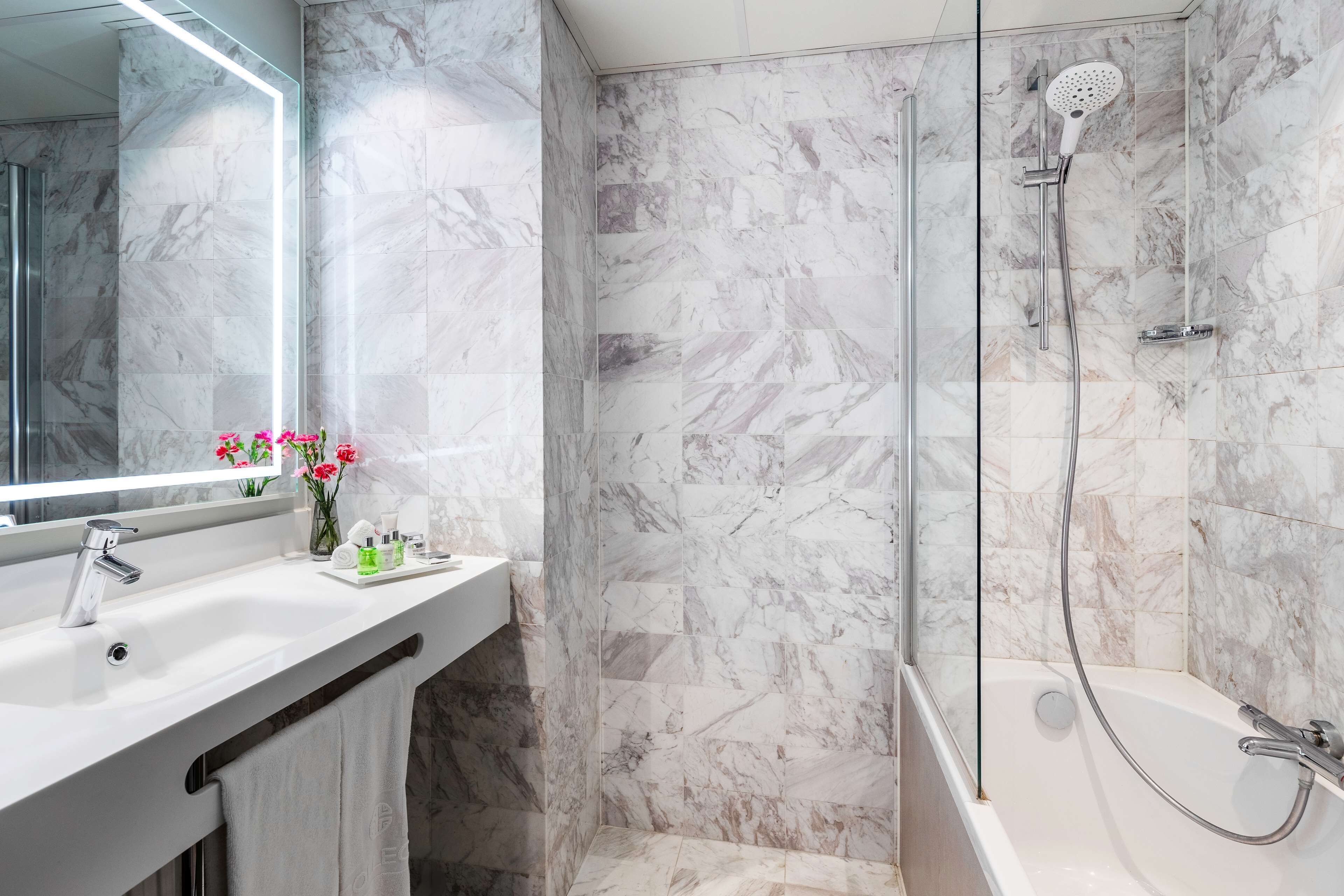 A modern bathroom with a marble shower and a sink with a mirror above it.