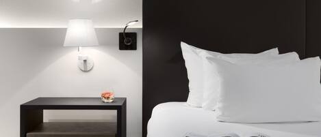 Una habitación de hotel moderna con una cama, una mesita de noche con lámpara y una revista sobre la cama.
