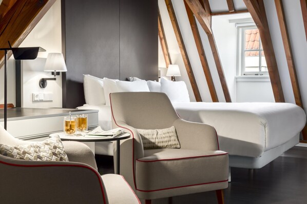 Une chambre d’hôtel moderne avec un grand lit, un bureau avec une lampe, une chaise et une petite table avec des boissons.