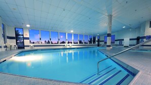 An indoor swimming pool with clear blue water, a tiled floor, and a view of the sunset through large windows. - Shilo Inn Suites Idaho Falls (Idaho Falls)