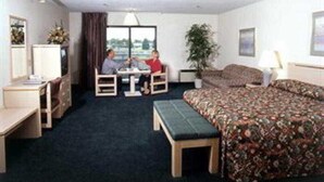 A hotel room with a bed, a desk, a chair, a small table, a sofa, a window, and a plant. - Shilo Inn Suites Idaho Falls (Idaho Falls)