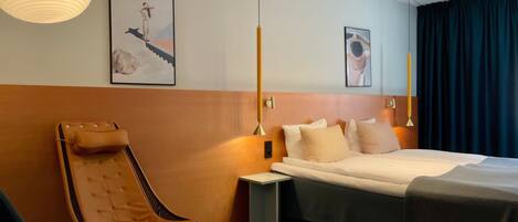 Una habitación de hotel moderna con una cama grande, una zona de estar con una silla, una mesita y obras de arte en las paredes.