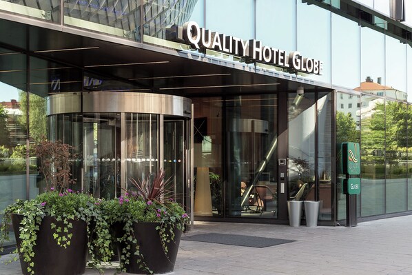 A modern hotel entrance with a revolving door, large glass windows, and potted plants. - Quality Hotel Globe (Johanneshov)