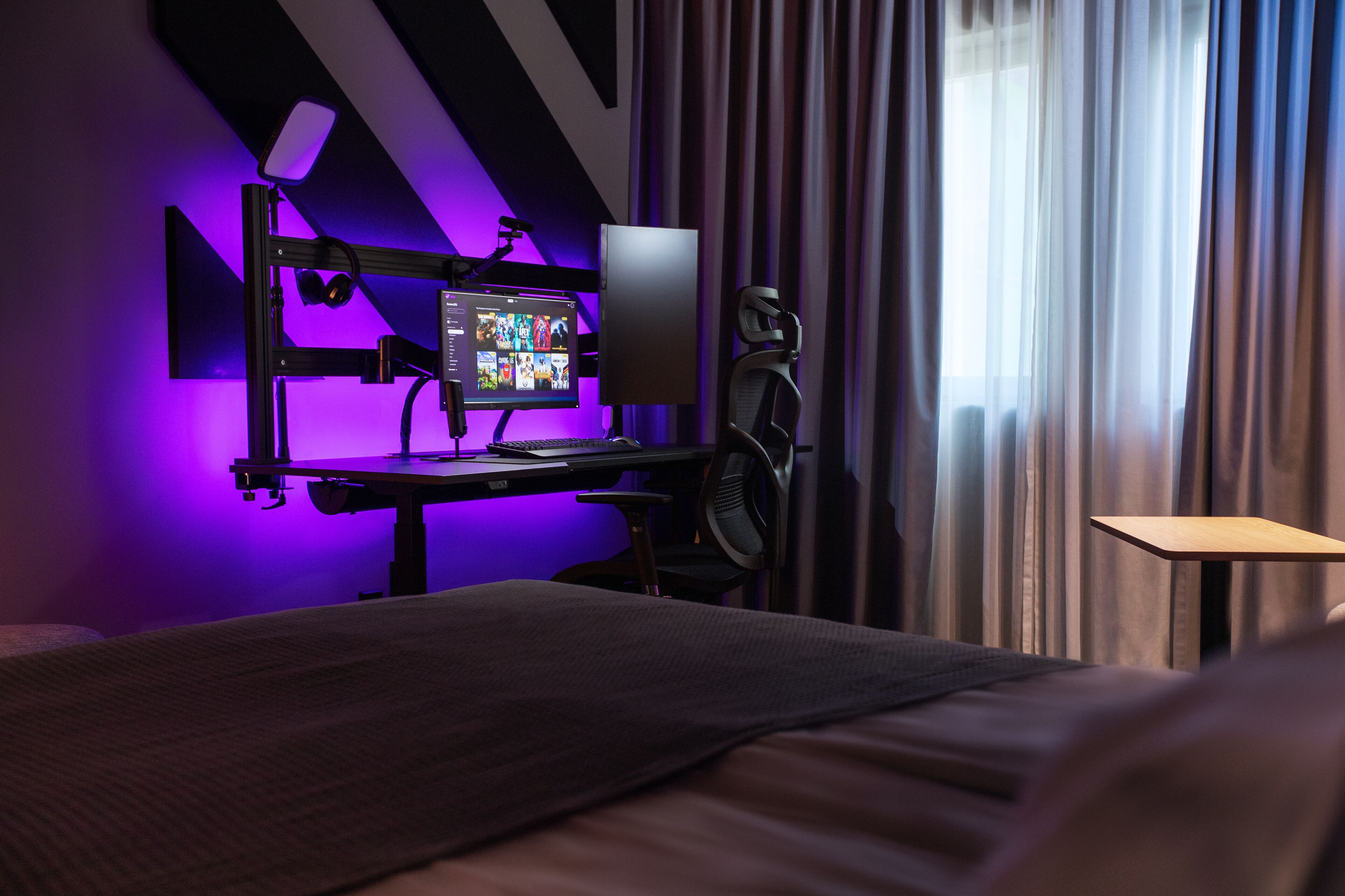 Ein modernes Hotelzimmer mit einem Bett, einem Schreibtisch mit Computer und Monitor, einem Ventilator und einem Fenster mit Vorhängen.