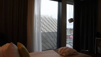 Ett hotellrum med ett stort fönster, en säng med kuddar och en hängande lampa.