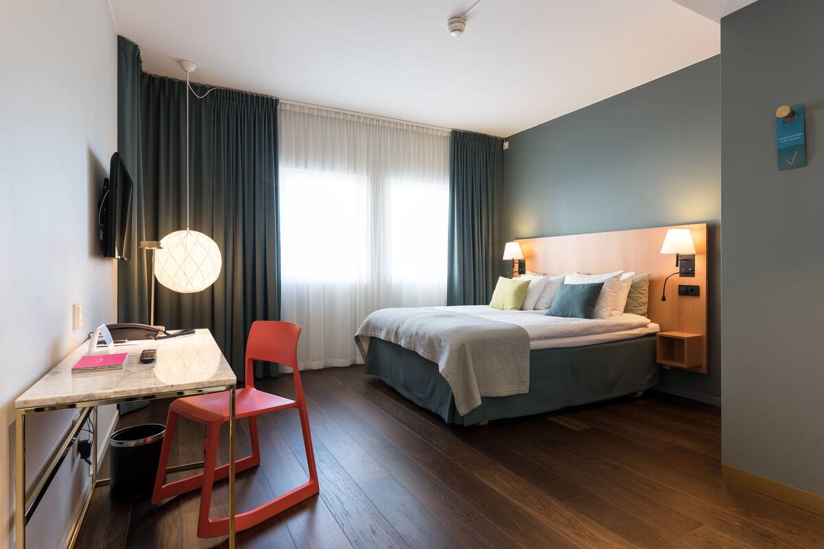 A modern hotel room with a bed, desk, chair, and two bedside lamps.