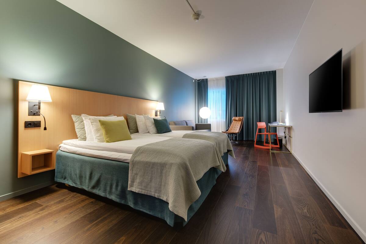 A modern hotel room with a large bed, bedside tables, a desk, and a TV.
