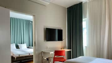 Habitación de hotel con dos camas, un escritorio, un televisor y una ventana con cortinas.