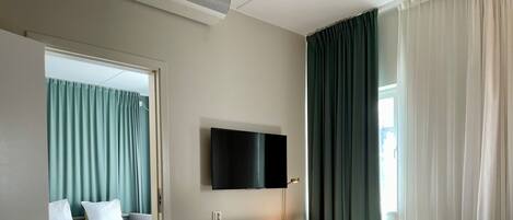 A hotel room with two beds, a desk, a TV, and a window with curtains.
