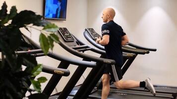 Un gimnasio con cintas de correr, una pantalla de televisión y una planta.