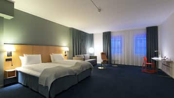 A hotel room with two beds, a desk, a chair, and a small table.