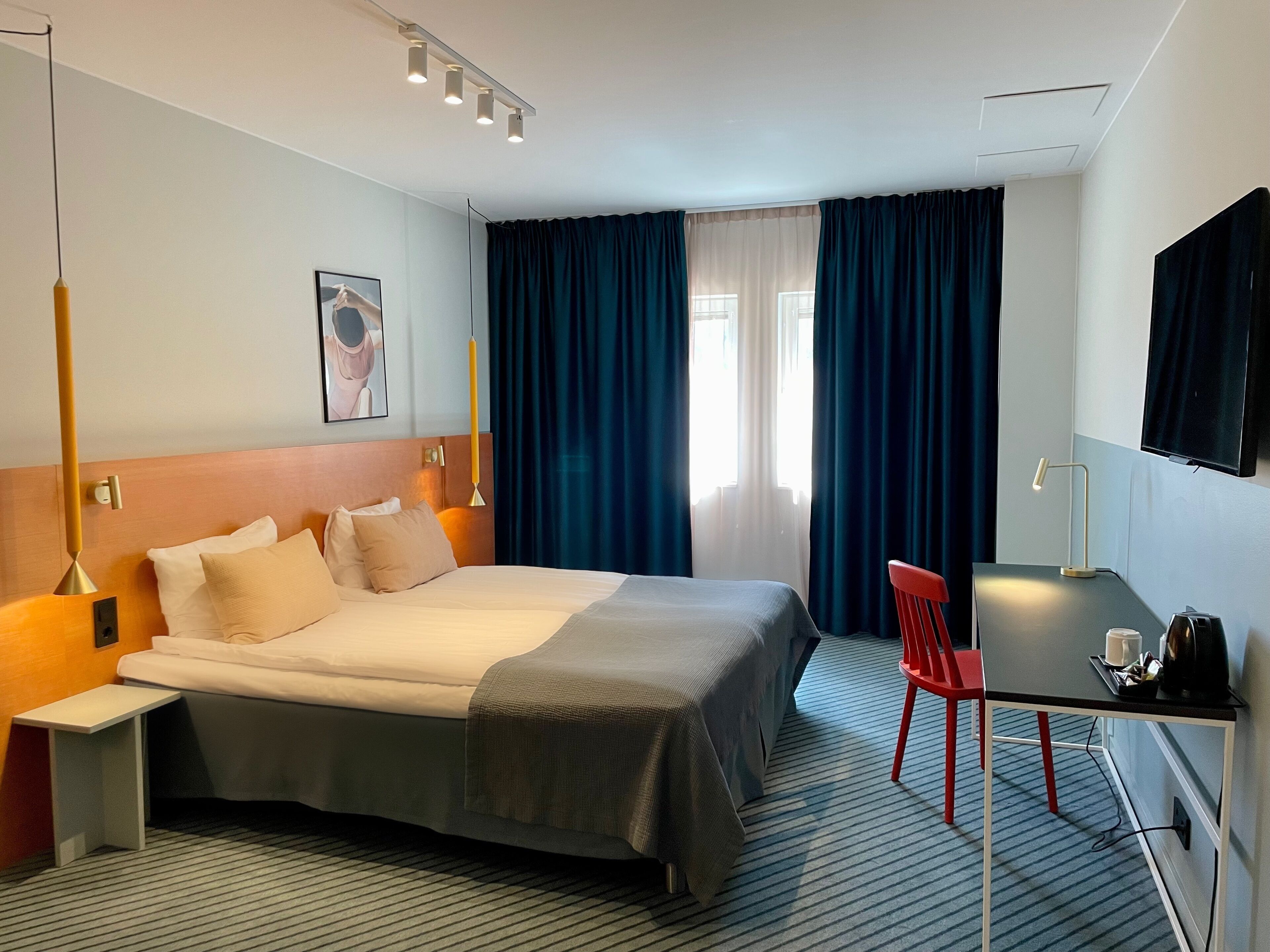 A hotel room with a bed, bedside table, lamp, desk, chair, and a TV.