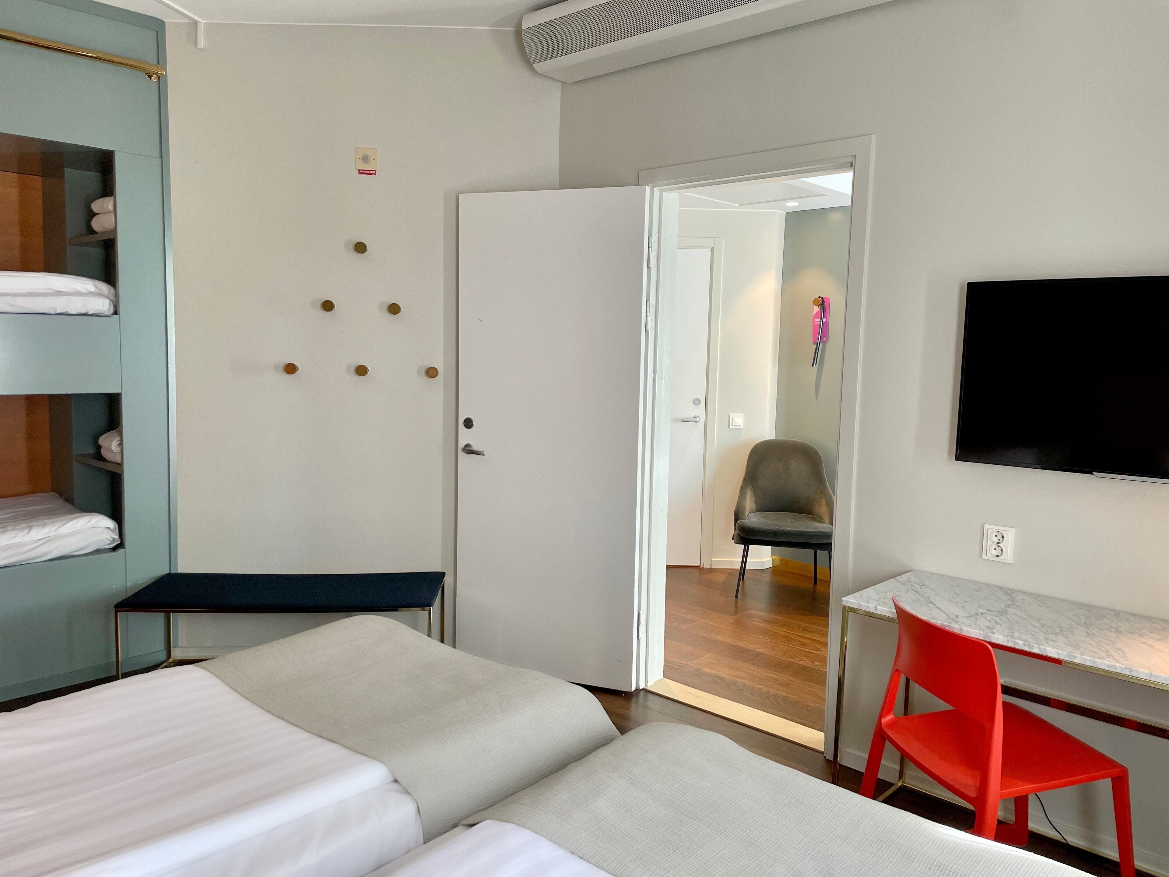 A hotel room with two beds, a desk, a chair, a TV, and a wardrobe.