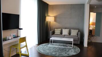 Una sala de estar moderna con un sofá gris, una mesa de centro blanca, una silla amarilla y un televisor de pantalla plana sobre un soporte blanco.