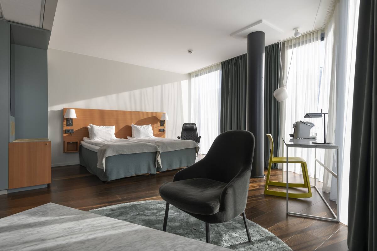 A modern hotel room with a large bed, a desk, and a chair.