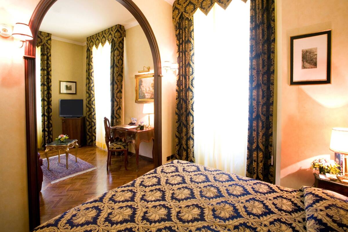 Habitación de hotel con una cama grande, un escritorio y una silla. Hay un espejo en la pared y un cuadro enmarcado.