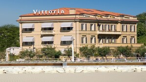 Un edificio con el nombre 'Vittoria' en la fachada, cerca de una playa con arena y agua tranquila.
