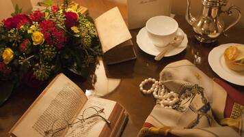 Un tavolo con un libro, occhiali, un bollitore, una tazza, una tazzina, un cucchiaino, un tovagliolo, un bouquet di fiori e un panno decorativo.