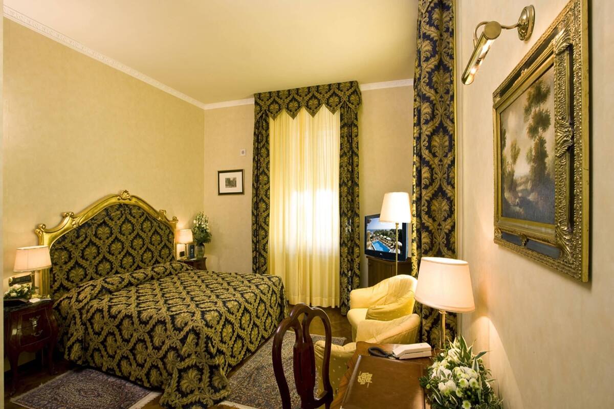 Habitación de hotel con una cama grande, una silla, un escritorio, un televisor y un cuadro en la pared.