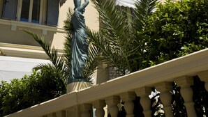 Un edificio con el nombre 'Vittoria' en la fachada, una estatua en primer plano y un balcón con barandilla.