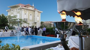 Un área de comedor junto a la piscina, con una fuente, mesas con comida y un edificio grande al fondo.