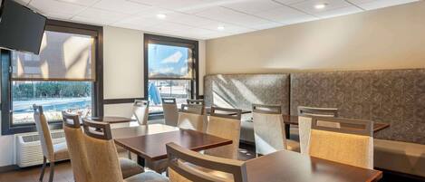 A restaurant with tables and chairs, a large window, and a television mounted on the wall.