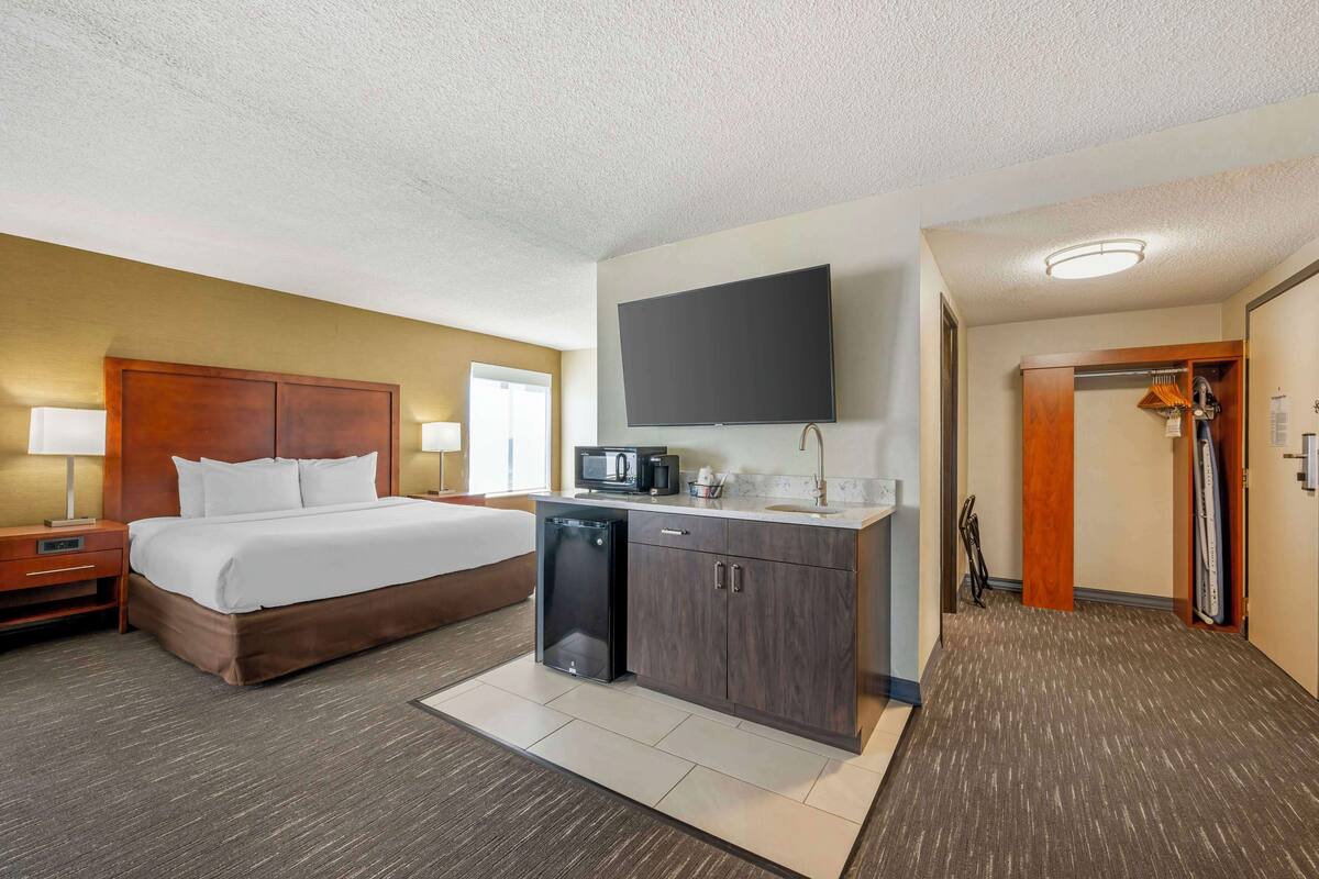 A hotel room with a bed, a small kitchenette, a flat-screen TV, and a walk-in closet.