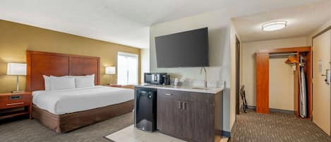 Habitación de hotel con cama, kitchenette pequeña, televisión de pantalla plana y vestidor.
