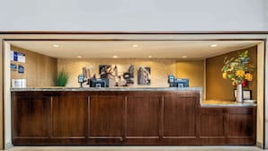 A reception desk with a stone wall backdrop, a plant, and a vase with flowers. - Best Western Chicago - Downers Grove (Downers Grove)