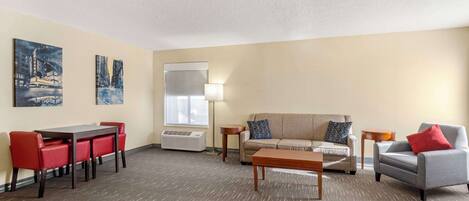A hotel room with a dining area, a sofa, a coffee table, and two side tables.