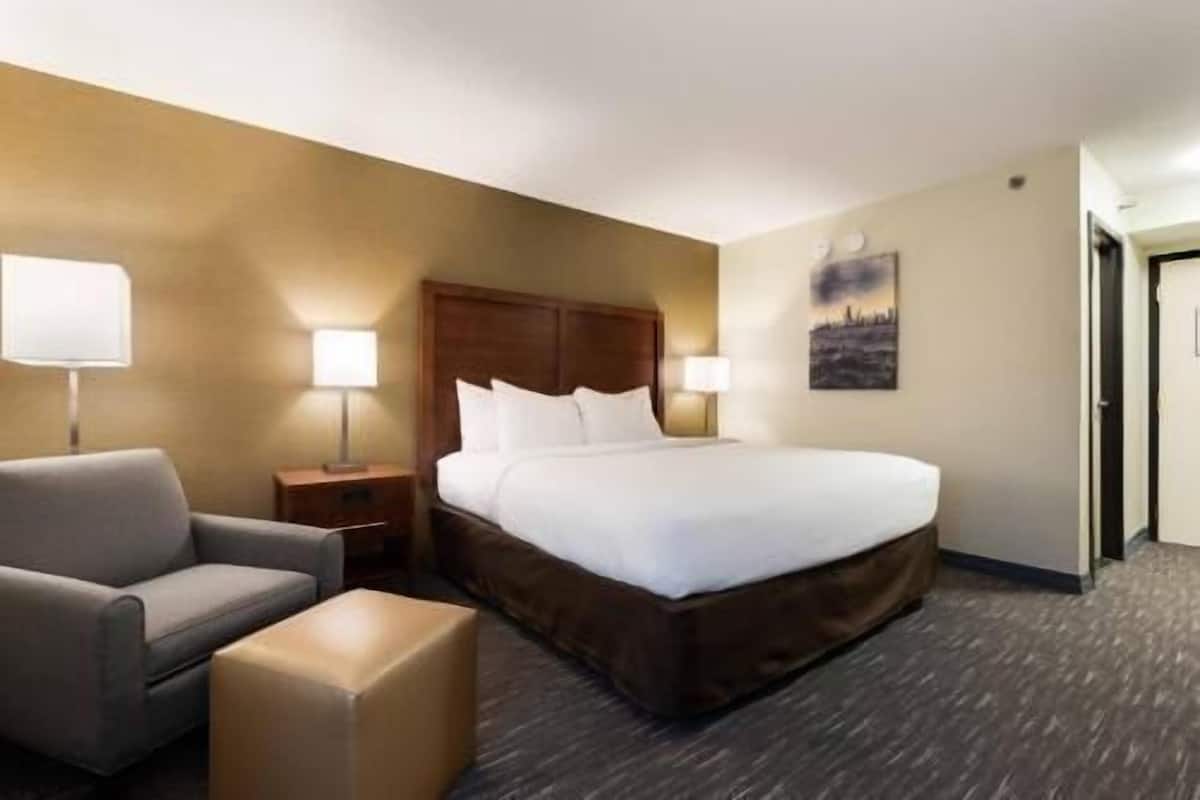 A hotel room with a bed, a chair, a nightstand, a lamp, and a painting on the wall.