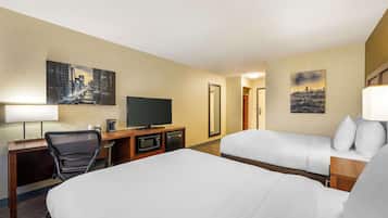 Ein Hotelzimmer mit einem großen Bett, einem Schreibtisch mit Fernseher, einem Sessel, einer Mikrowelle und einer Kaffeemaschine. An den Wänden hängen zwei Bilder.