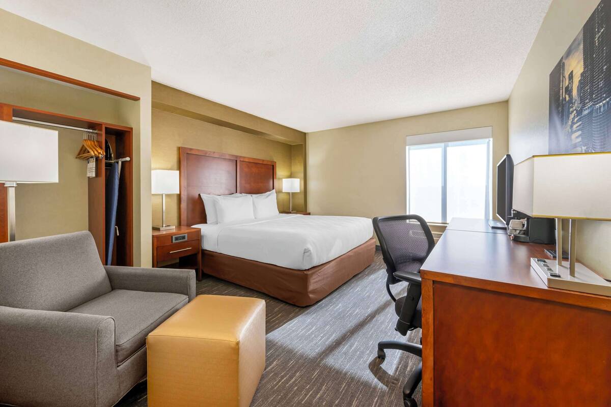 A hotel room with a bed, a desk, a chair, a sofa, and a window.