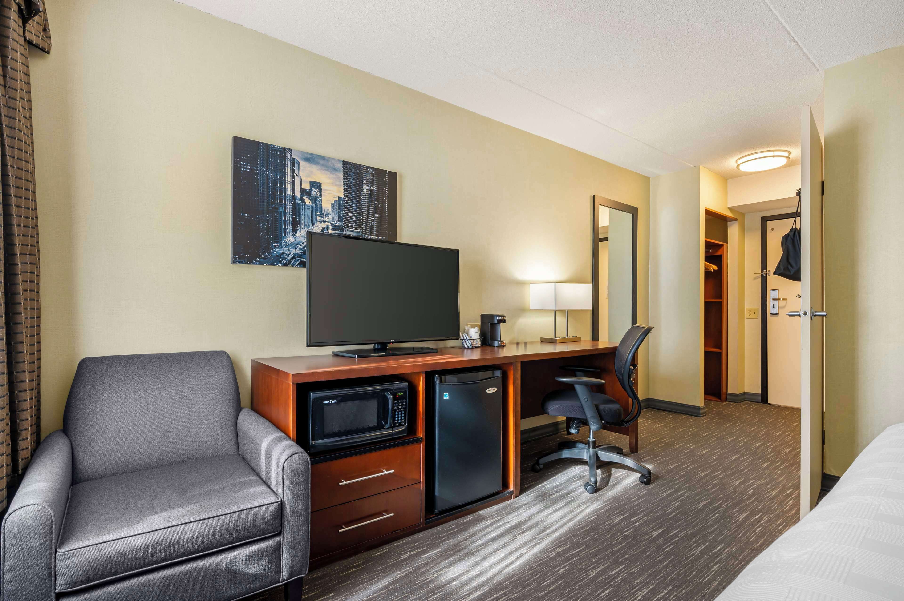 Habitación de hotel con sofá, escritorio, televisor de pantalla plana, microondas, refrigerador pequeño y cama.