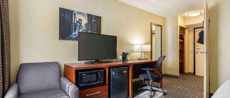 A hotel room with a sofa, a desk with a flat-screen TV, a microwave, a mini-fridge, a chair, and a bed.