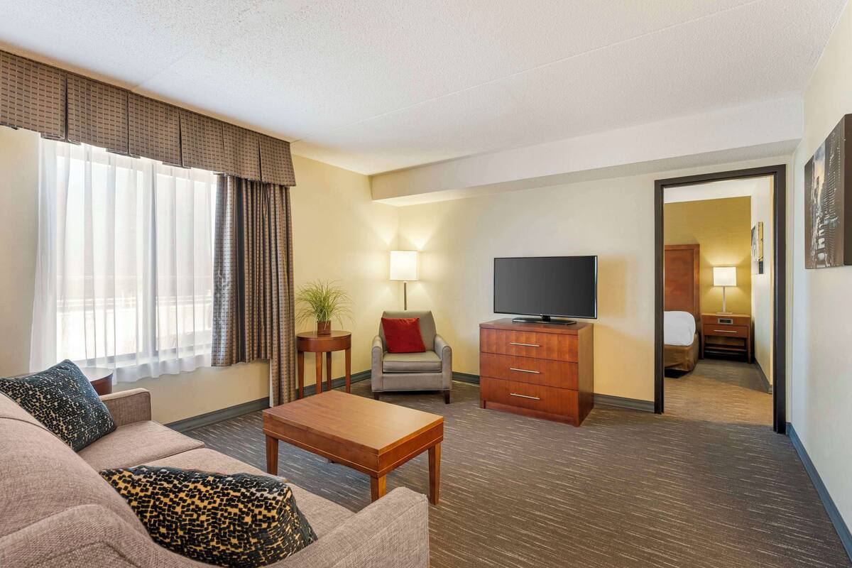 A hotel room with a sofa, a coffee table, a TV, a desk, and a lamp.