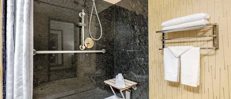 Un baño moderno con ducha de vidrio, paredes de mármol y un perchero con toallas dobladas.
