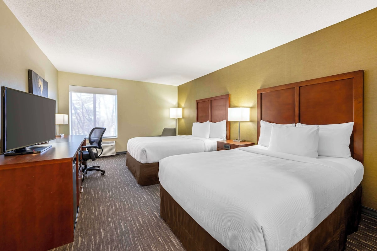 A hotel room with two beds, a desk with a television, and a chair.