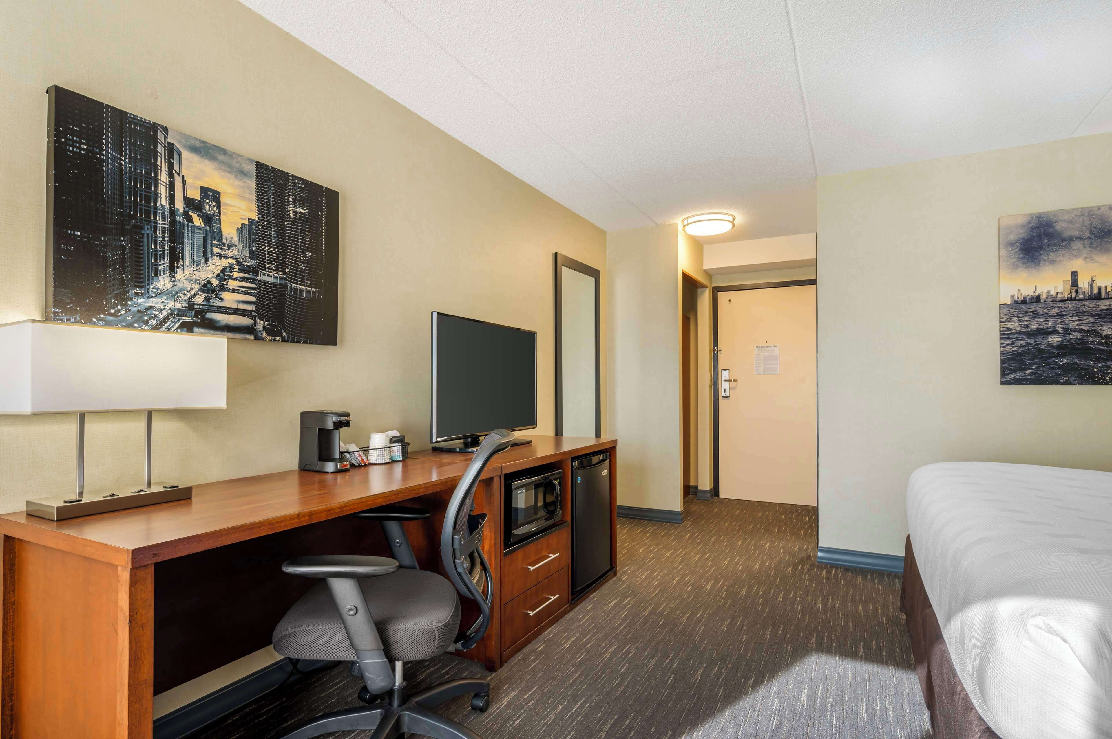A hotel room with a wooden desk, a television, a microwave, and a bed.