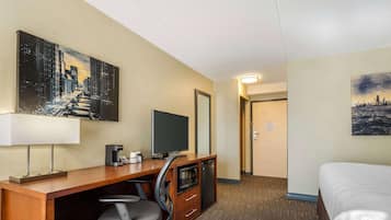 A hotel room with a wooden desk, a television, a microwave, and a bed.