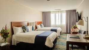A hotel room with two beds, a desk, a chair, a TV, and a window with curtains. - The Voyager Inn (Anchorage)