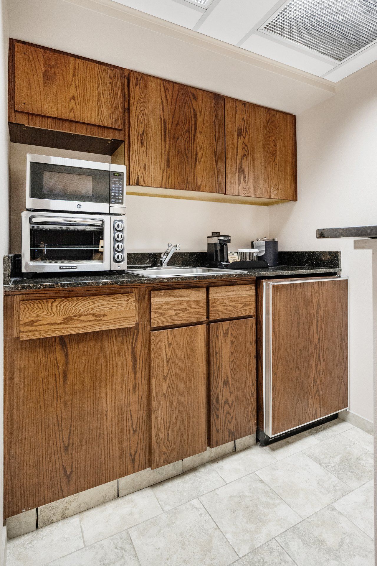 Una cocina con armarios de madera, un microondas, un horno, un lavamanos y un refrigerador.