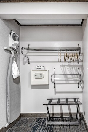 Un baño de hotel con un perchero para toallas, una plancha, un secador de manos, un dispensador de toallas y un banco.